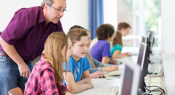 Schülergruppe die zusammen mit einem Lehrer am Laptop arbeitet